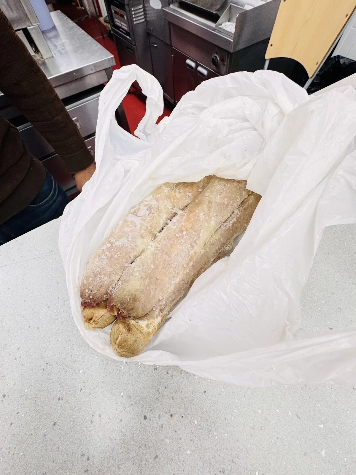 A wrapped submarine roll in a white bag resting on the counter
