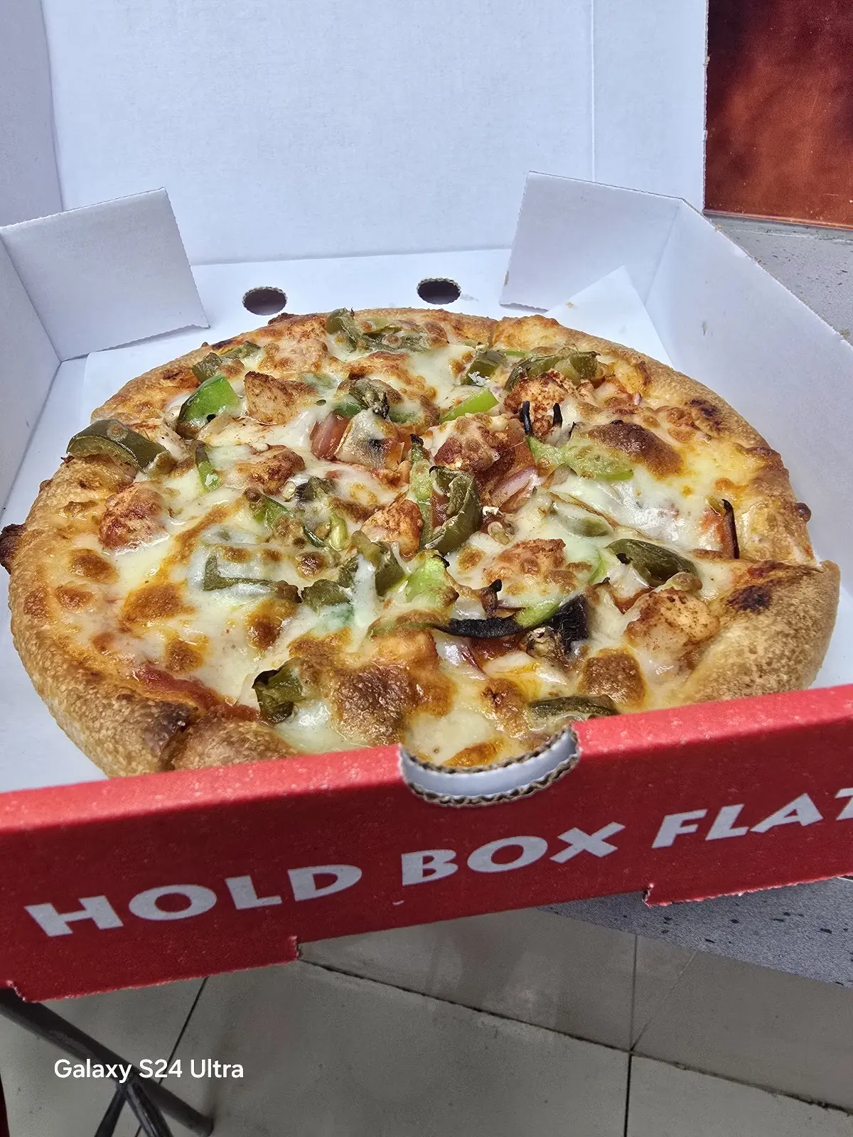 A freshly baked vegetable-topped pizza in an open red takeaway box