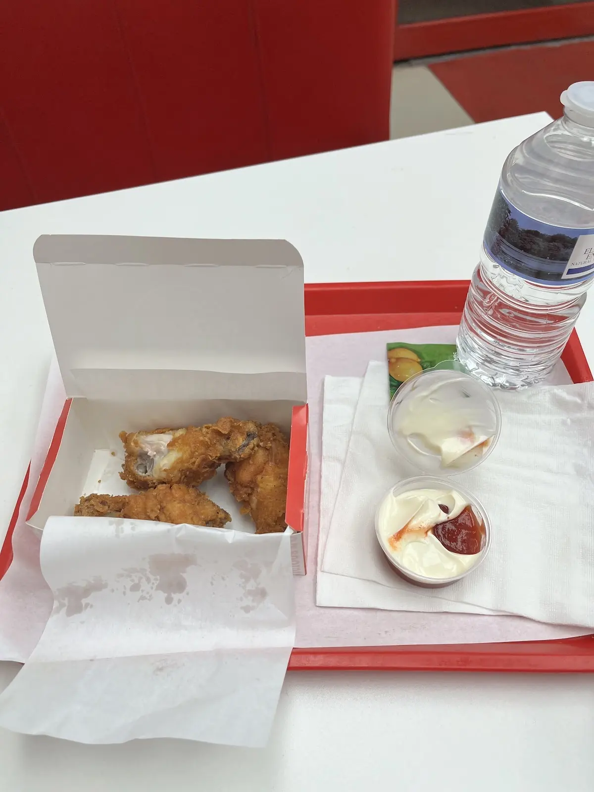 A tray of fried chicken pieces with dips, a salad pot and a bottle of water